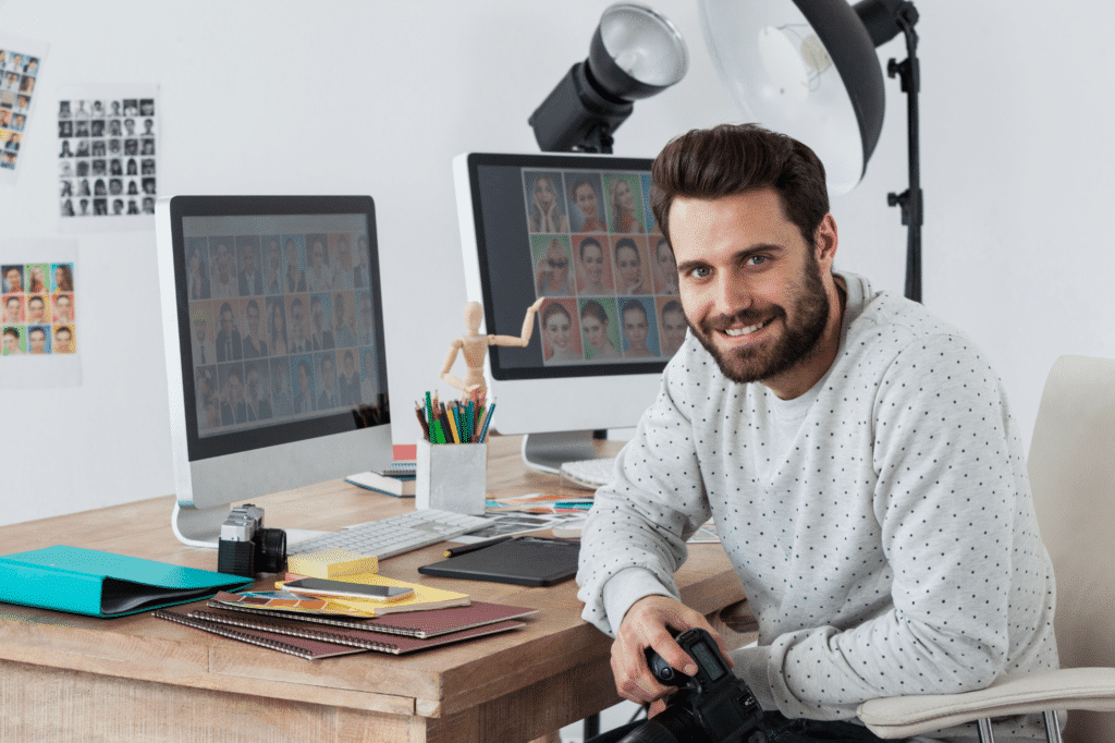 happy-photographer-holding-camera-at-his-desk-2023-11-27-05-13-24-utc